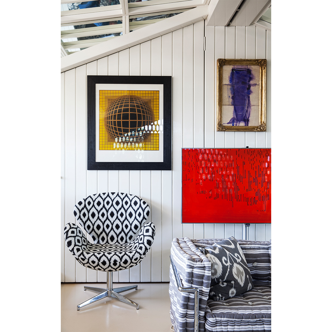 paintings on a wall over optical armchair and sofa
